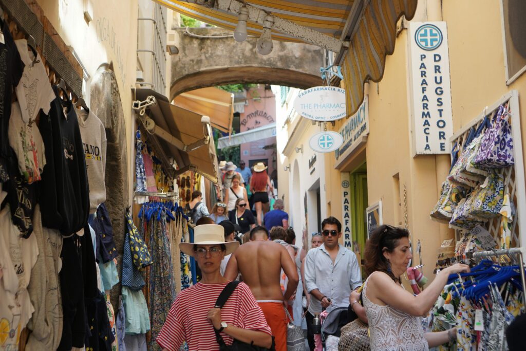 Travelers walking through a bustling local alley filled with shops, tourists, and locals on the Amalfi Coast.
